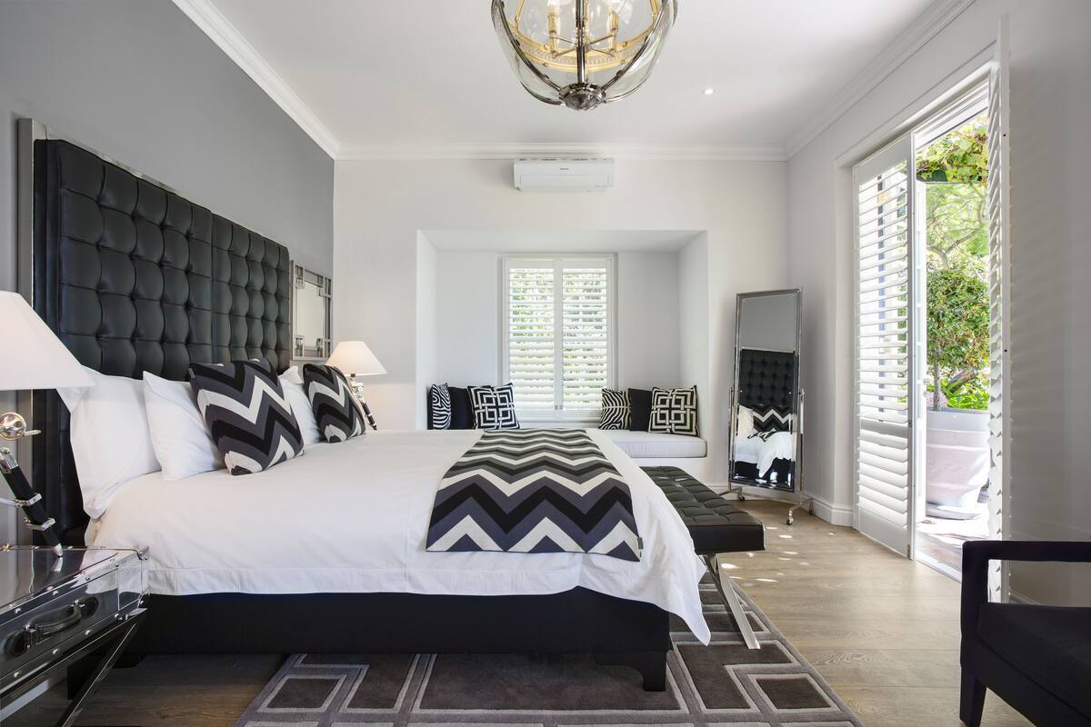 A modern bedroom with a large bed, a chandelier, and a view of the outdoors through a window.