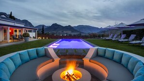 A modern outdoor pool area with a fire pit, lounge chairs, and a view of mountains. - La Providence Guest House & Wine Farm (Franschhoek)
