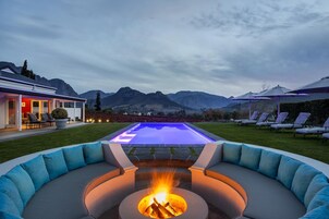 Un área de piscina moderna al aire libre con una chimenea, sillas de descanso y vistas a las montañas.