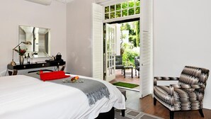 A hotel room with a bed, a desk with a mirror, a chair, and an open door leading to a patio with outdoor furniture. - La Providence Guest House & Wine Farm (Franschhoek)