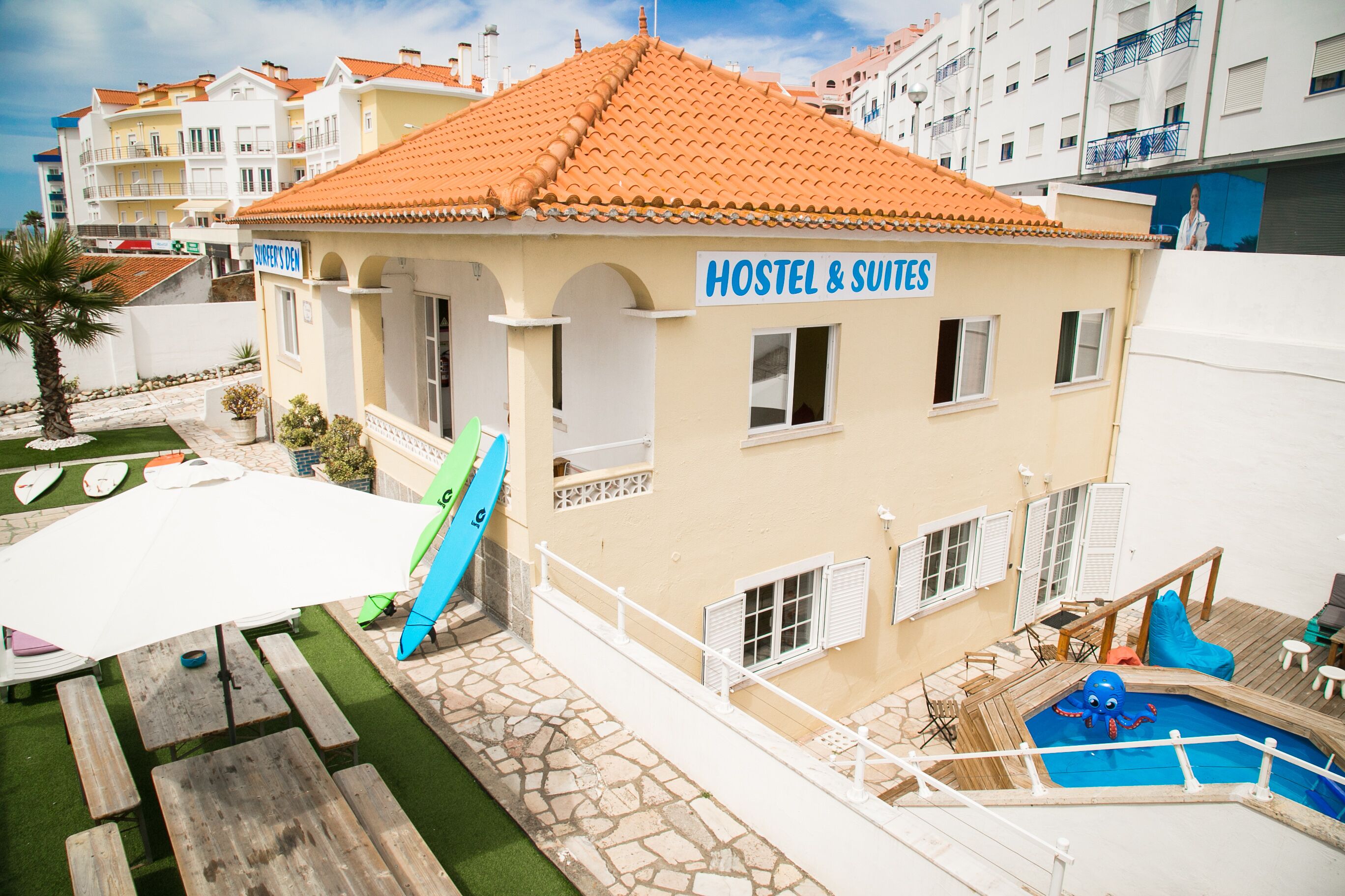 Un hostal con piscina, asientos exteriores y un cartel que indica que ofrece habitaciones de hostal y suites.