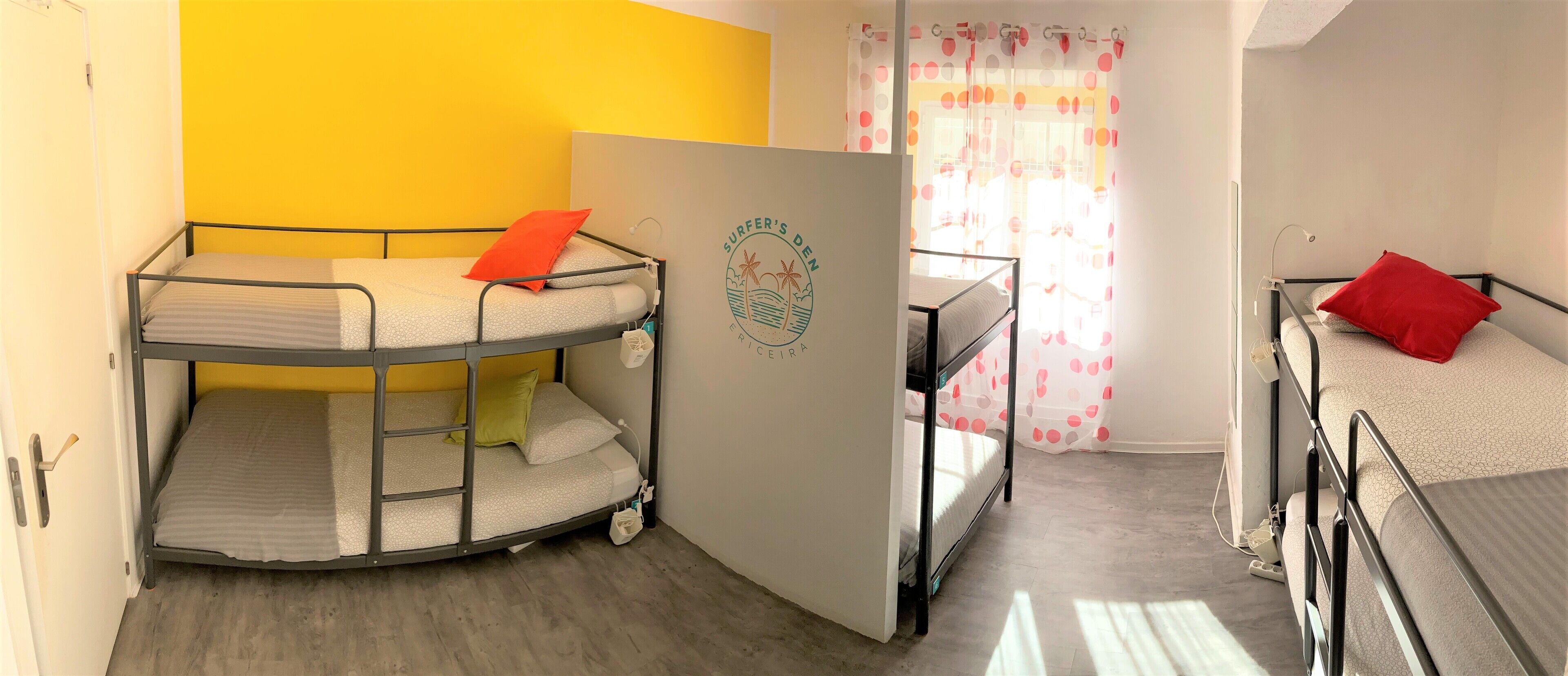 Ein Zimmer mit Etagenbetten, einer Tür mit einem Logo und einem Fenster mit Vorhängen.