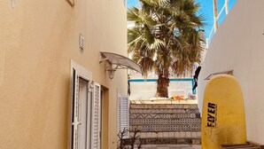 A narrow alleyway with a palm tree, a yellow surfboard, and a tiled staircase leading to a building. - Surfer's Den Ericeira (Mafra)