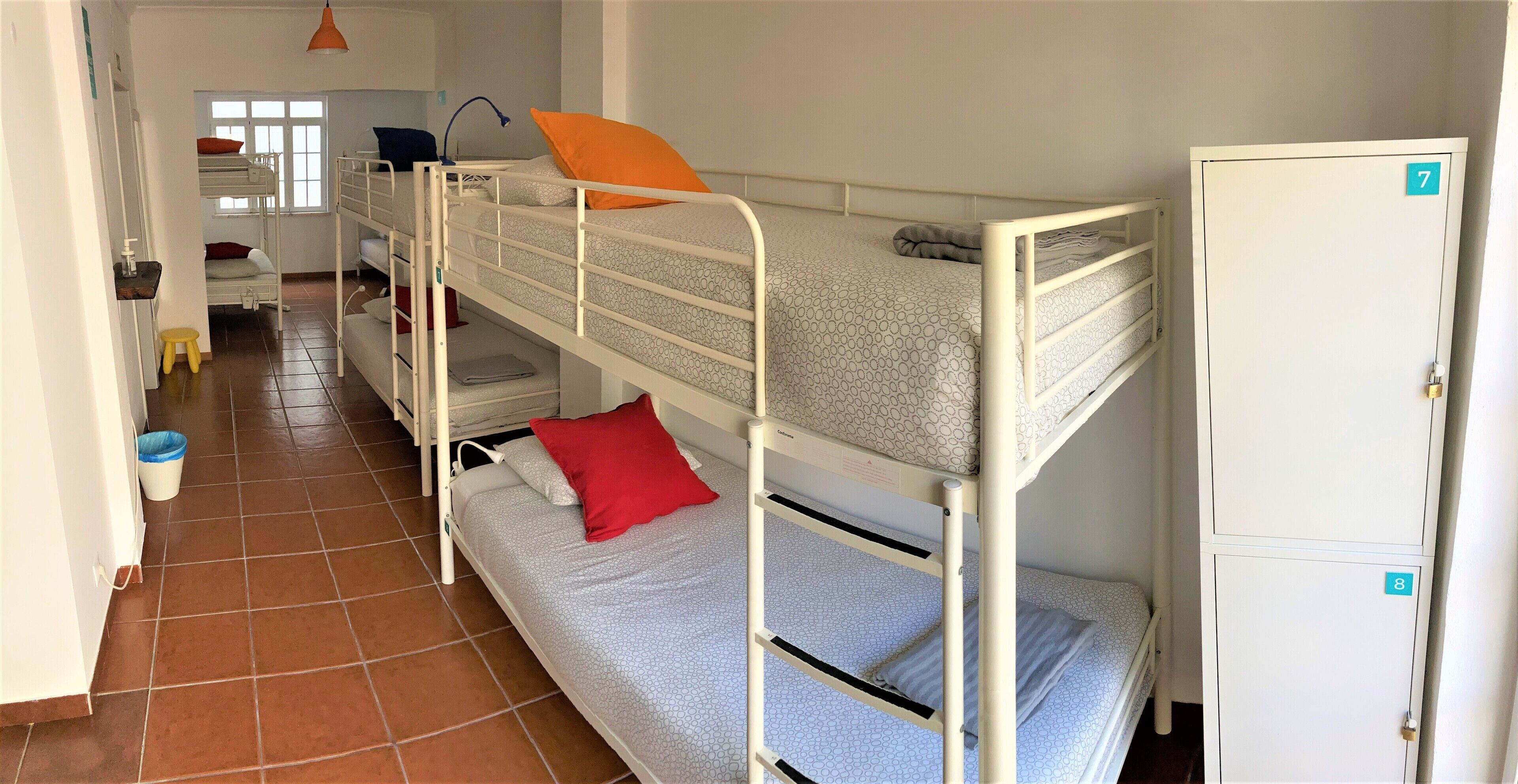 A dormitory room with bunk beds, a desk, a chair, a window, and a wardrobe.