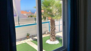A window with a view of a palm tree and artificial grass outside. - Surfer's Den Ericeira (Mafra)