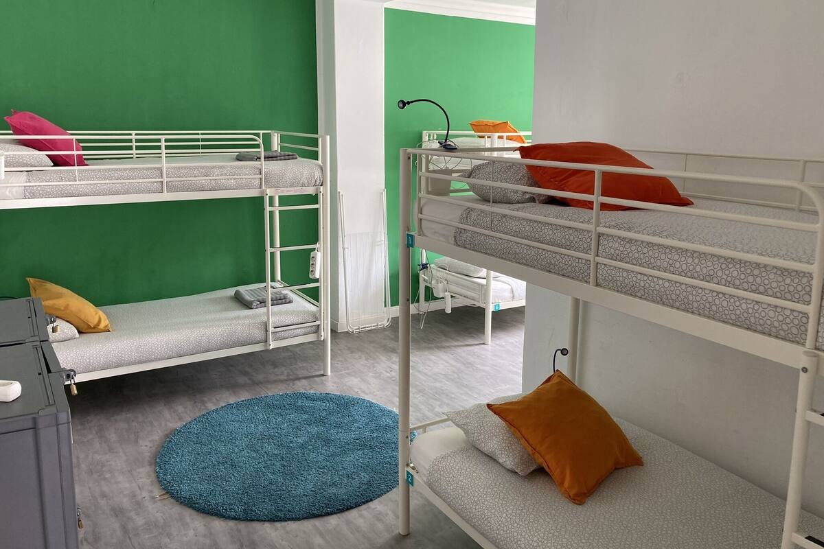 Een slaapkamer met een stapelbed, groene wanden, een blauw vloerkleed en een witte radiator.