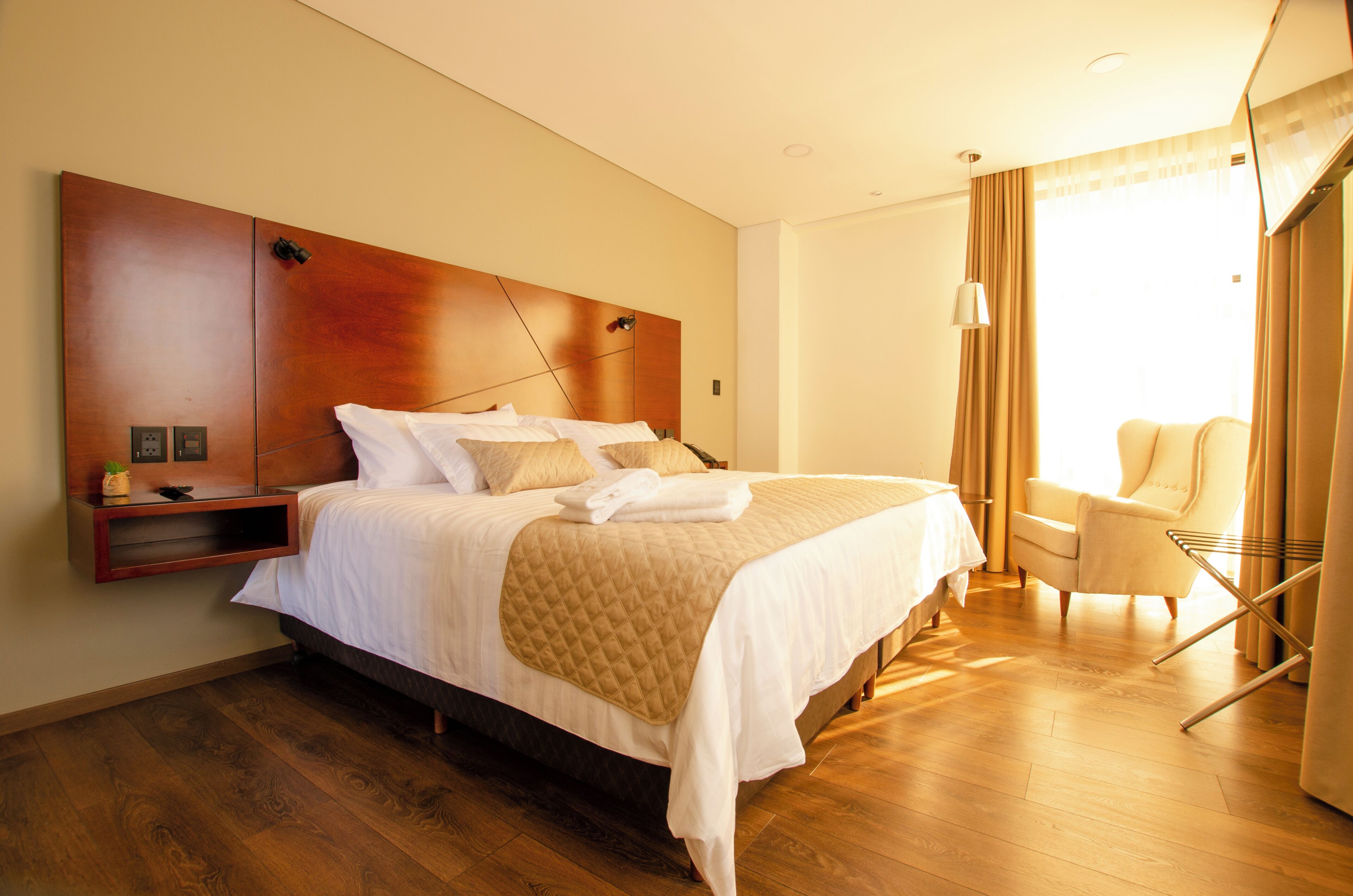 A hotel room with a large bed, a bedside table, a chair, and a window with curtains.
