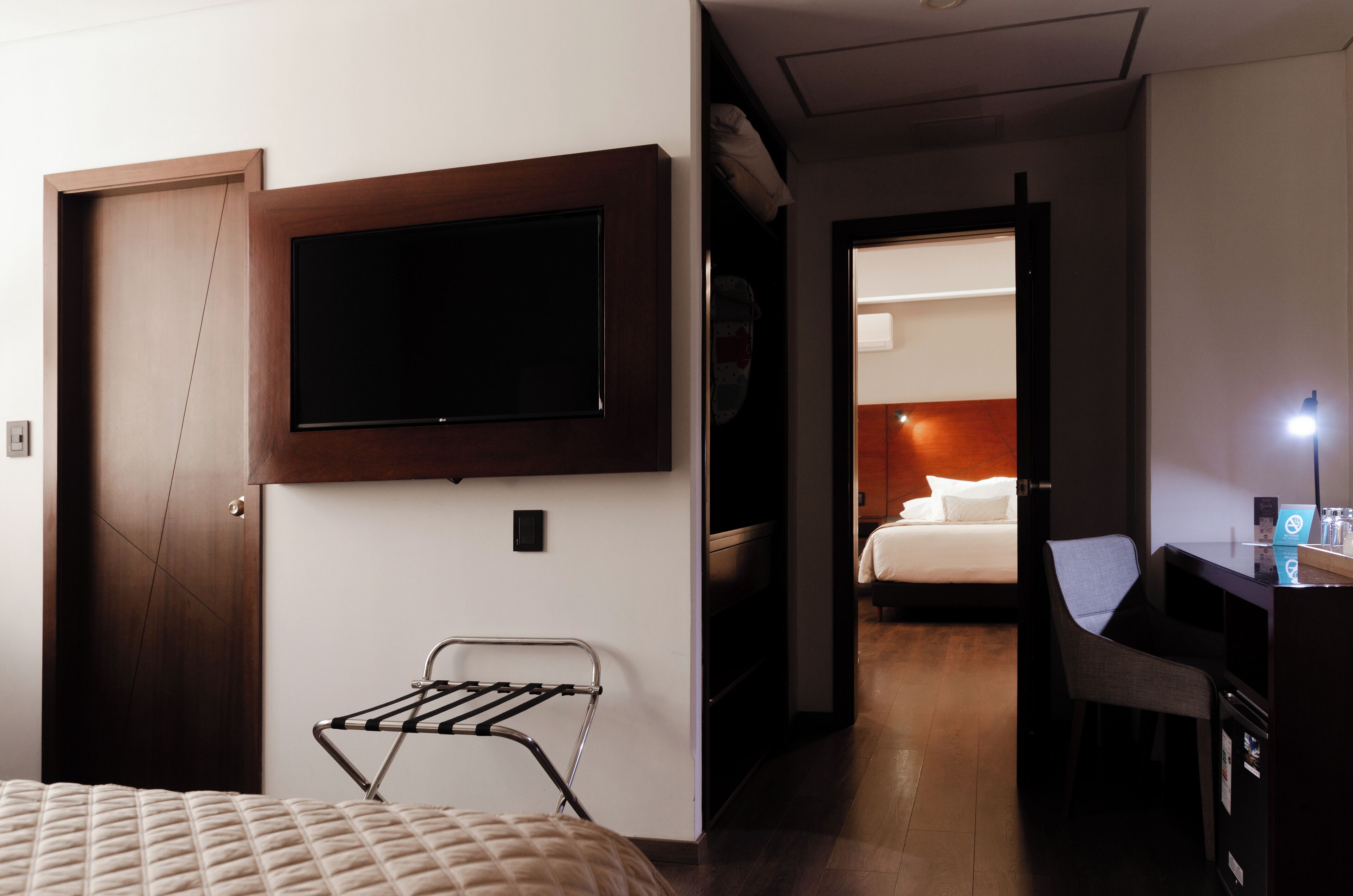 A hotel room with a bed, a TV mounted on the wall, a desk with a chair, and a walk-in closet.