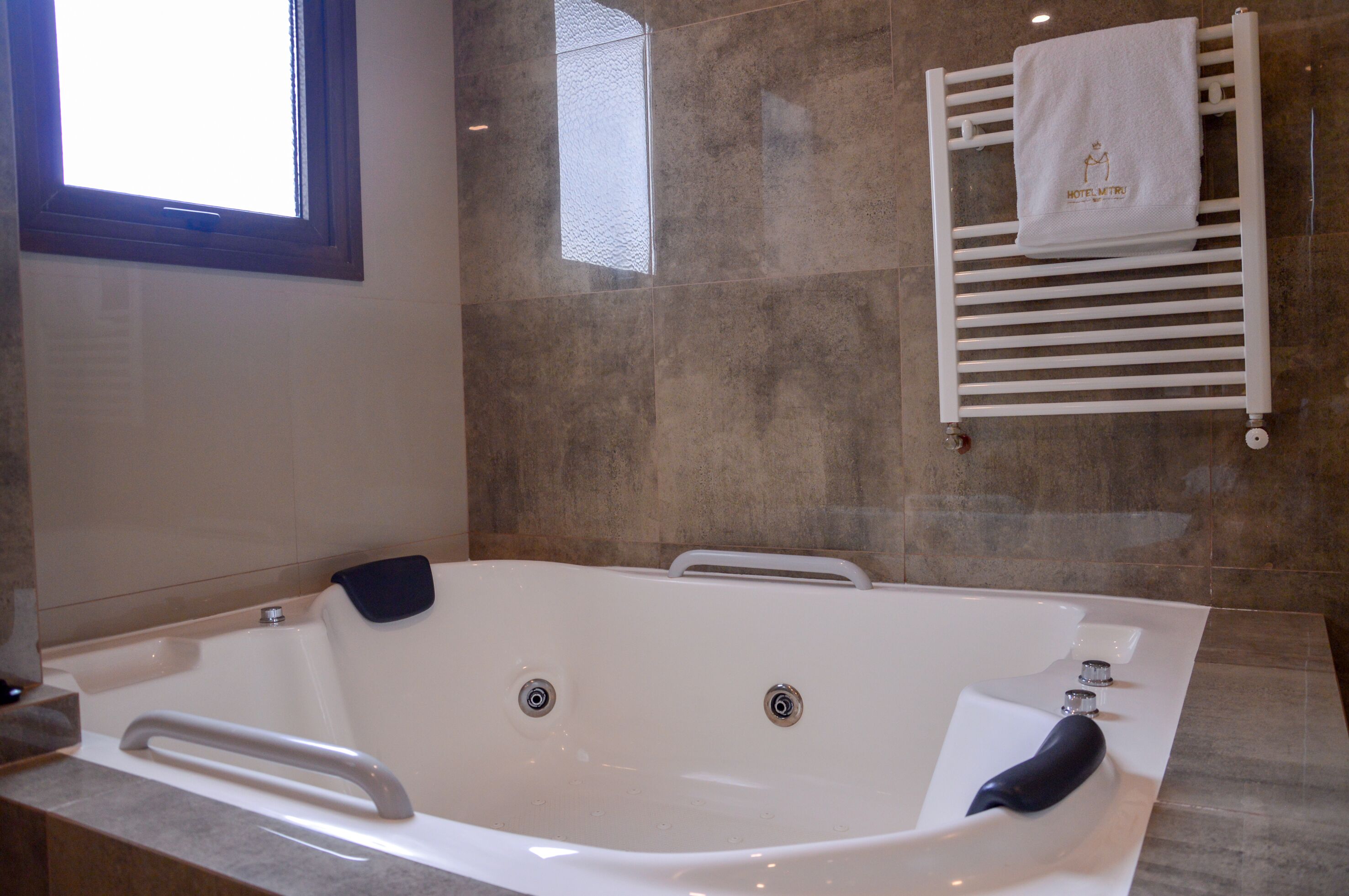 A modern bathroom with a large bathtub, a towel rack with a towel, and a window.