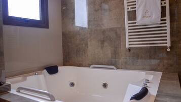 A modern bathroom with a large bathtub, a towel rack with a towel, and a window.