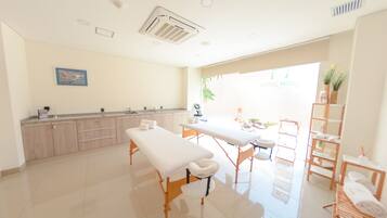 A clean, well-lit room with a reception desk, a massage table, and a small seating area.