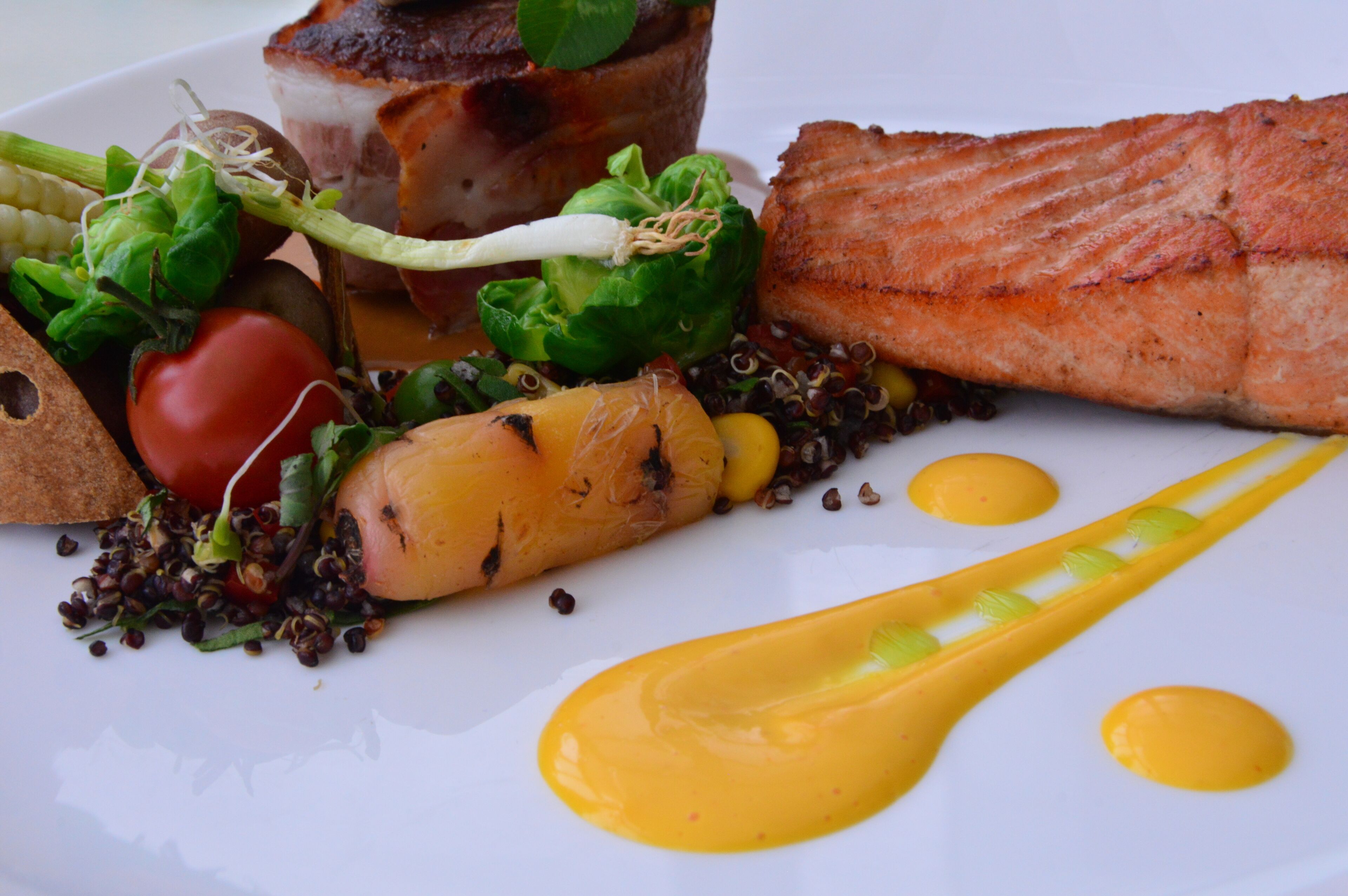 Une assiette de nourriture comprenant du saumon, des légumes et une sauce.