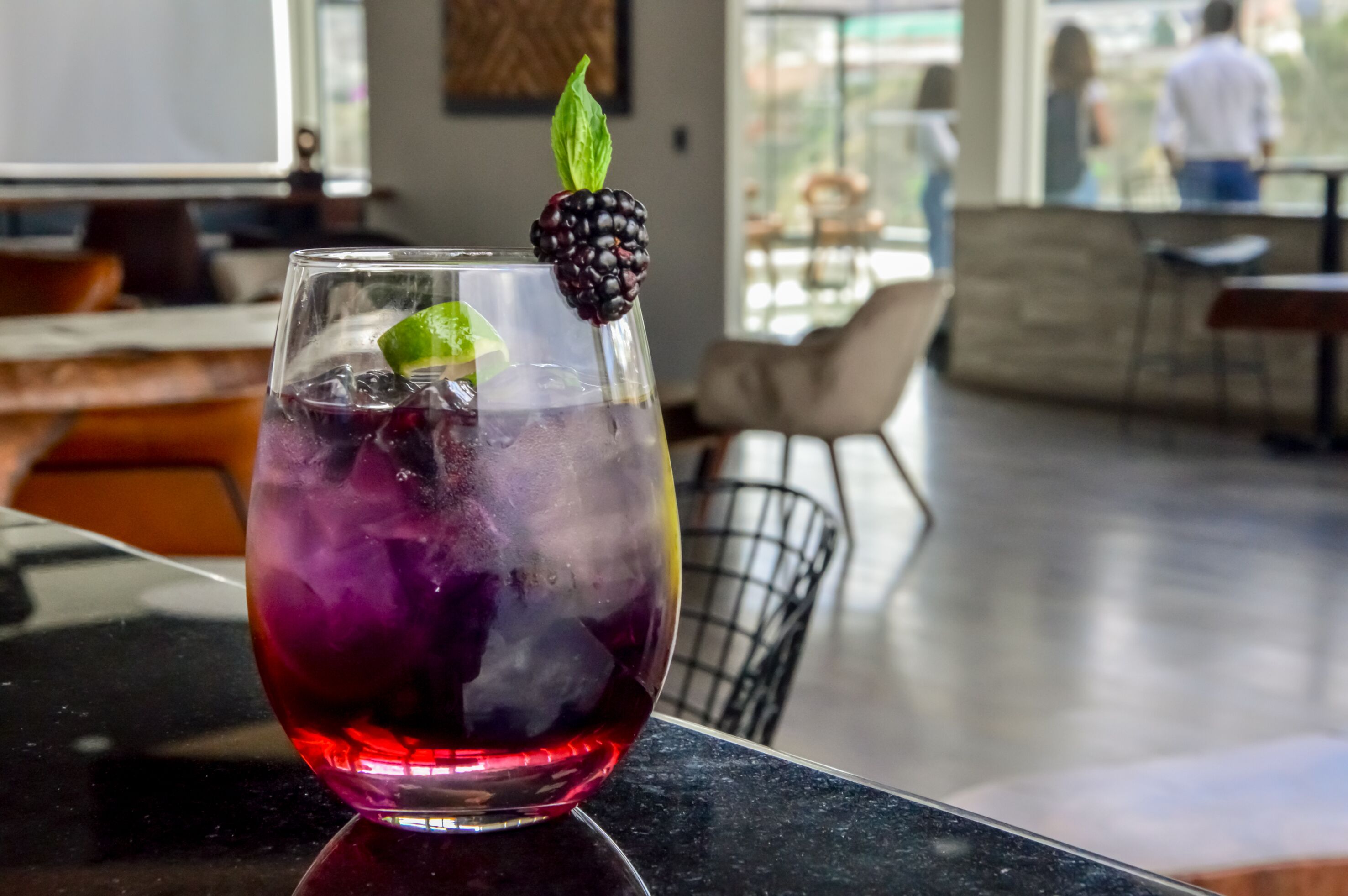 A glass of purple drink with ice and a blackberry garnish on a bar counter.