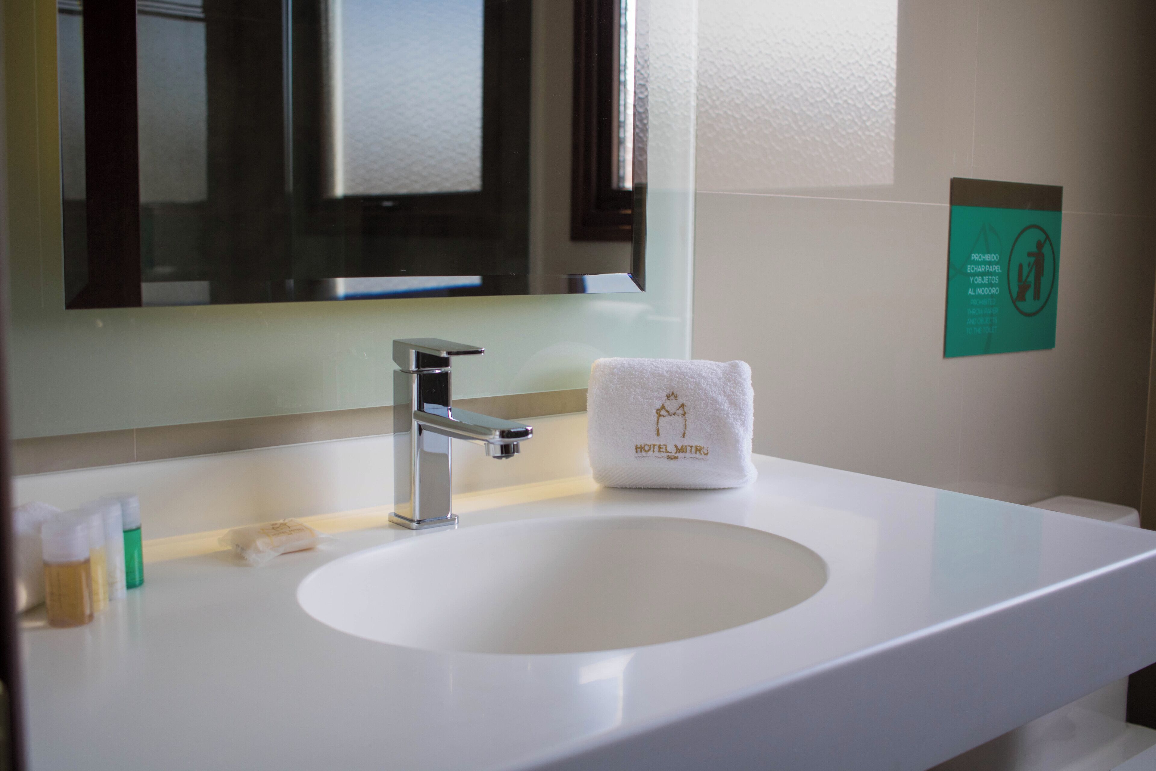 Ett hotellbadrum med en vit handfat, en spegel och en handduk med hotellets logotyp.