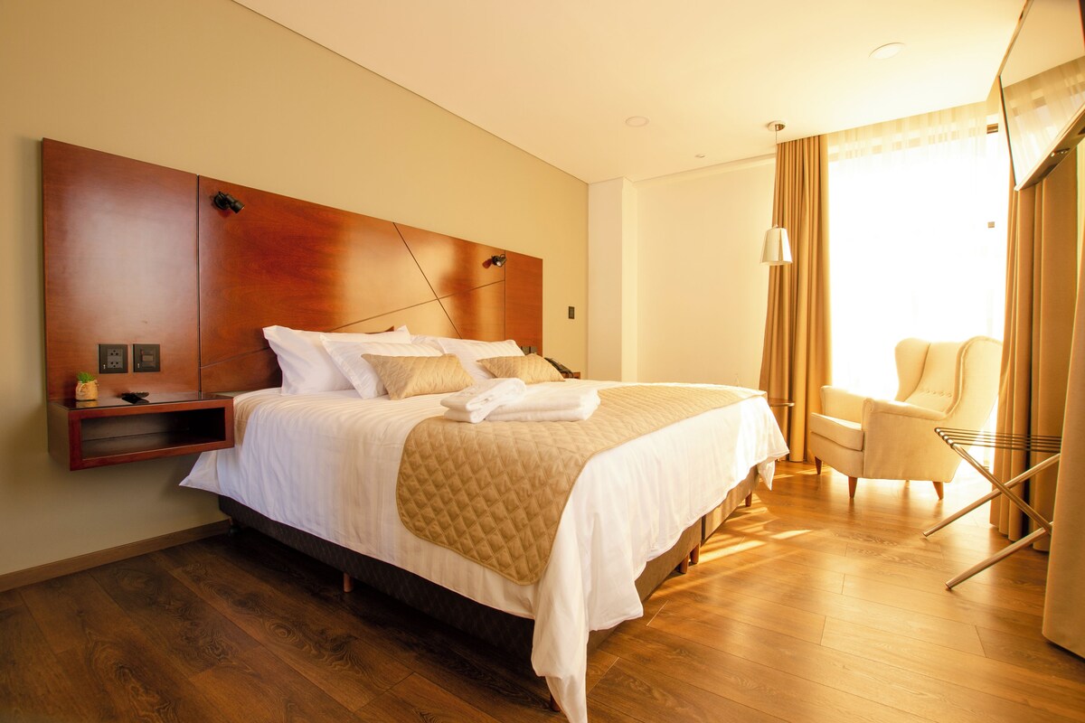 A hotel room with a large bed, a bedside table, a chair, and a window with curtains.
