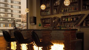 A bar area with a brick counter, hanging pendant lights, and a view of a building through large windows.