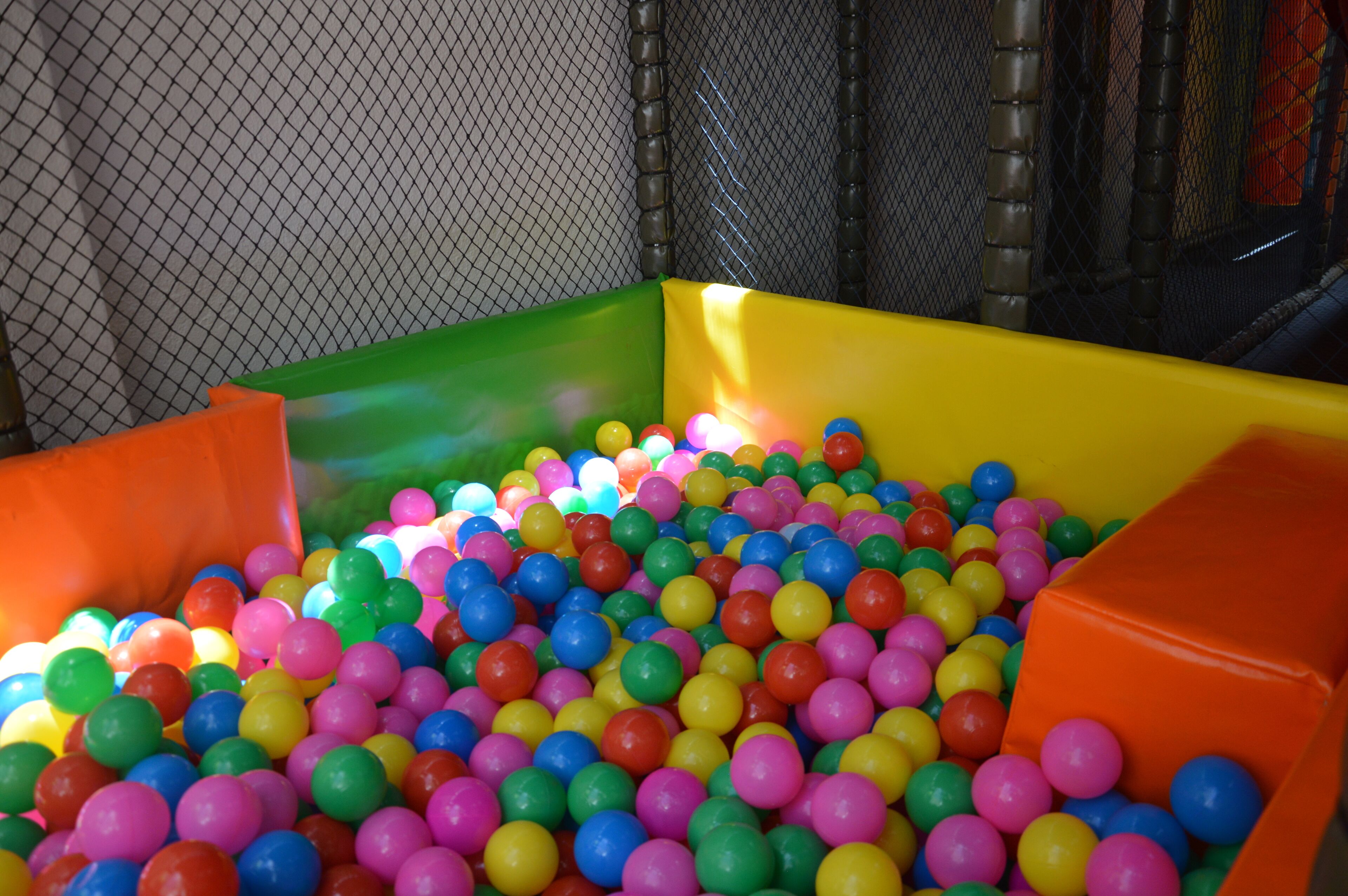Una piscina de pelotas coloridas con pelotas de varios colores y una cerca de malla al fondo.