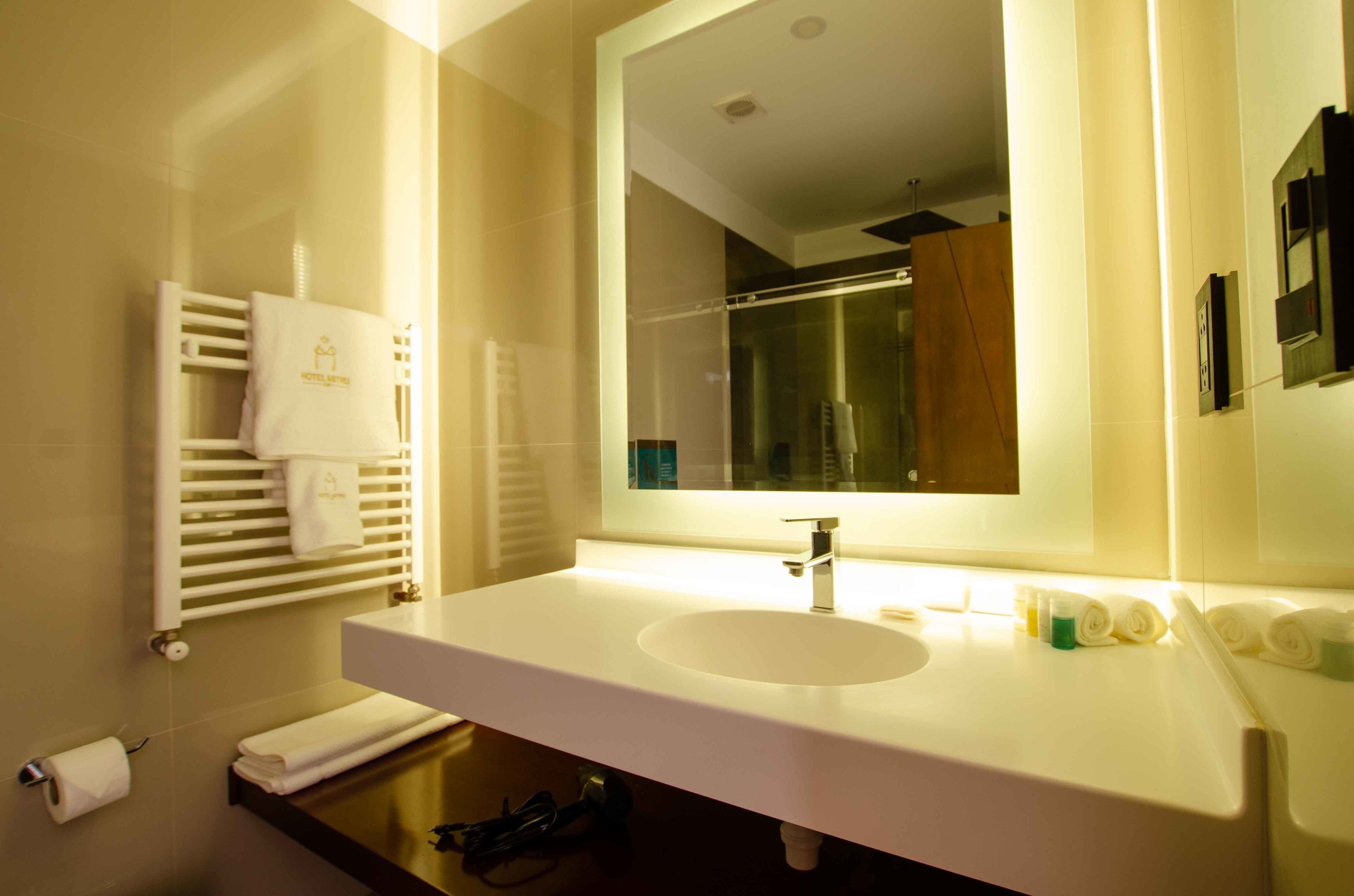 A modern bathroom with a white sink, a large mirror, and a towel rack with a white towel.