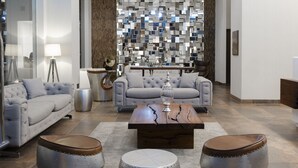 A modern living room with a grey sofa, two round ottomans, a coffee table, and a decorative wall with a mosaic pattern.