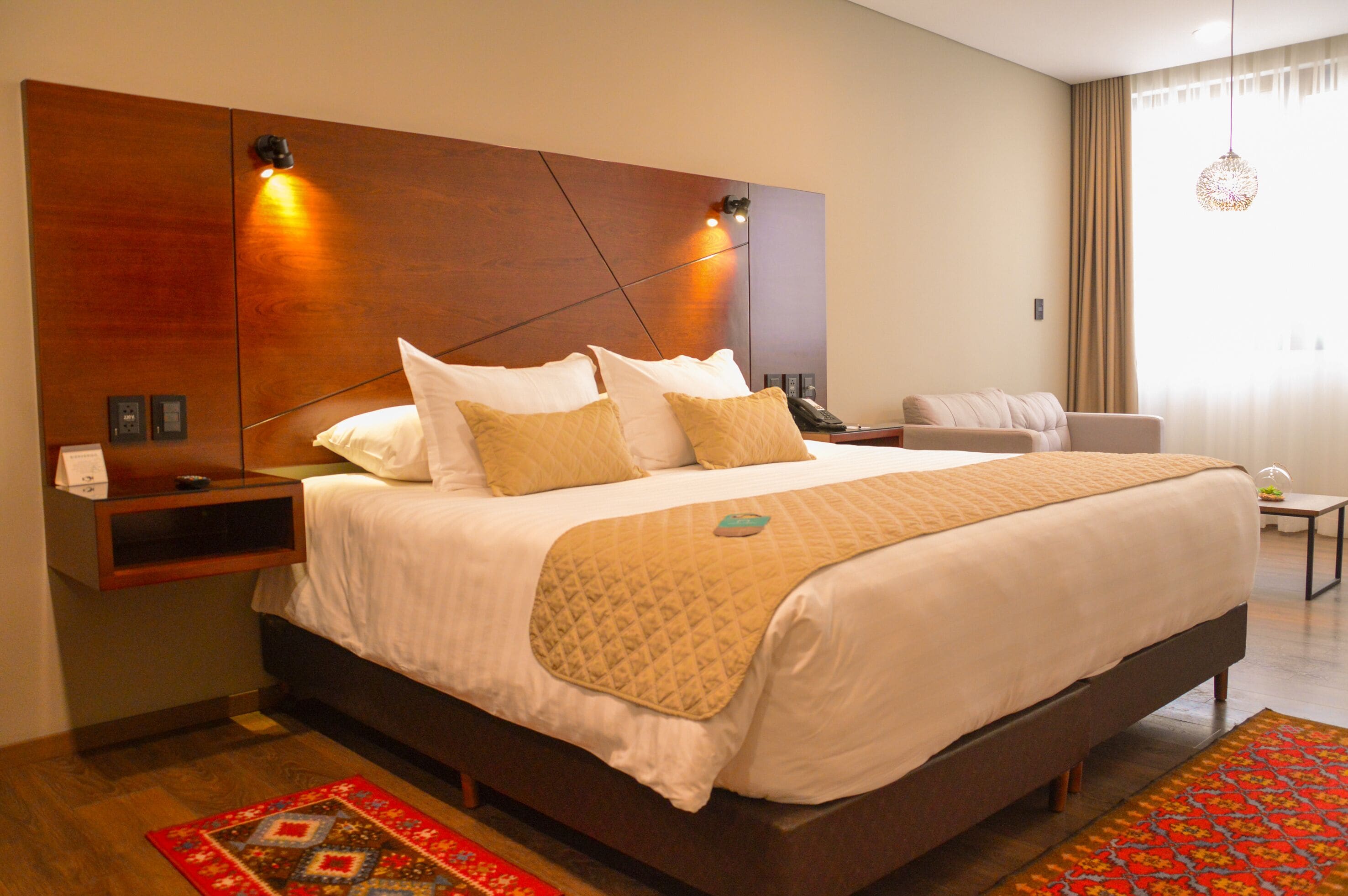 A modern hotel room with a large bed, a bedside table, a nightstand, a chair, and a window with curtains.