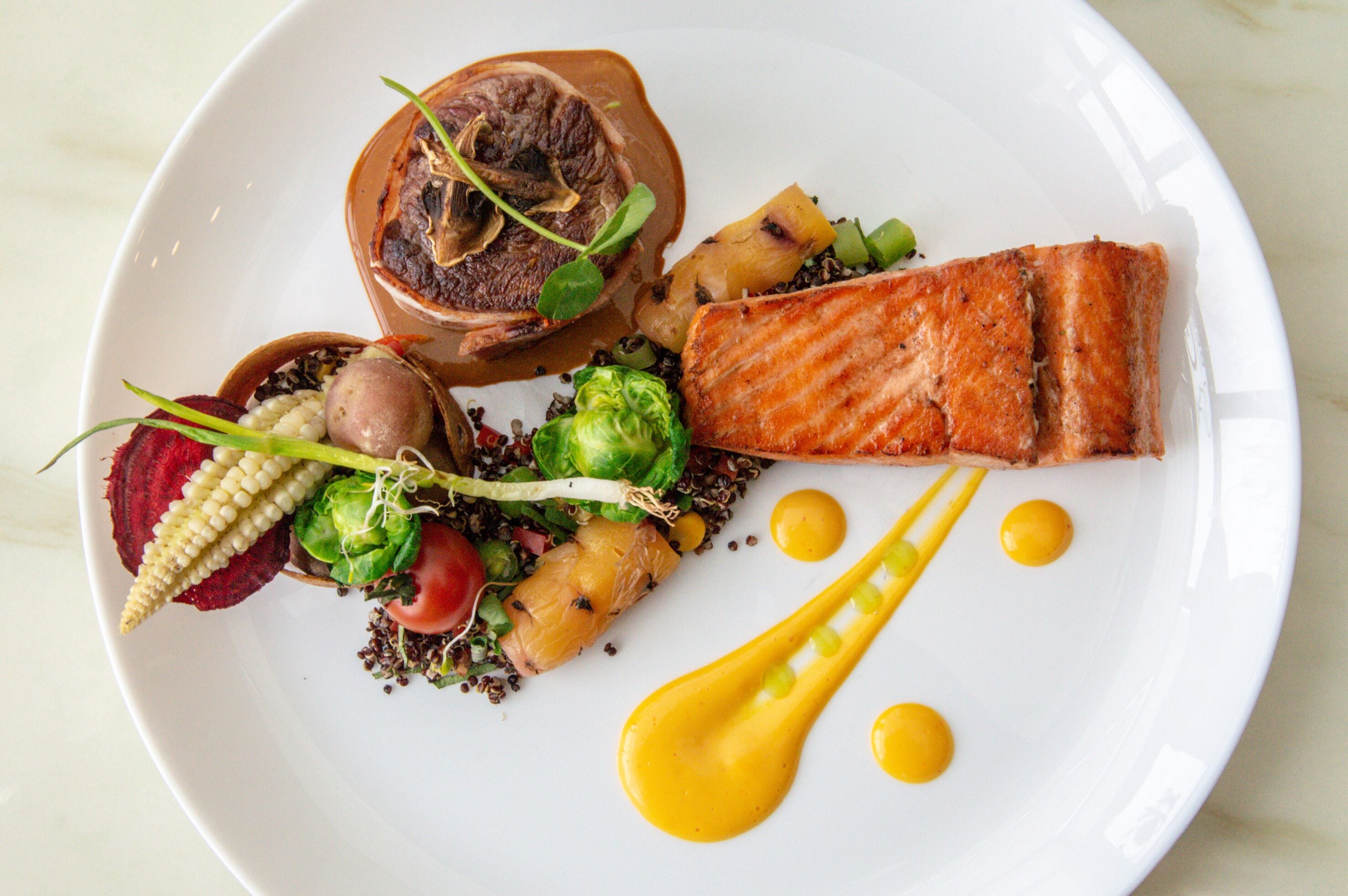A plate of food with various items including salmon, vegetables, and a sauce.