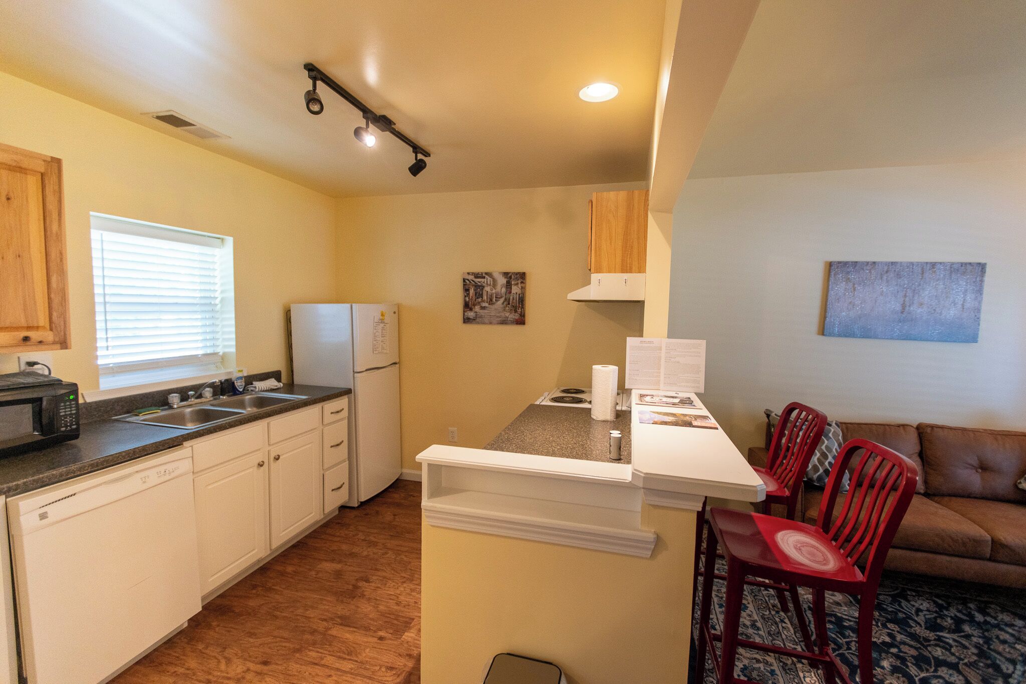 A compact kitchen with white cabinets, a microwave, and a refrigerator. There is a small dining area with a table and two red chairs.