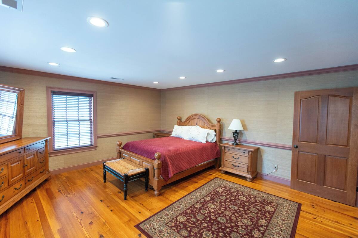 A bedroom with a wooden bed, a nightstand, a dresser, a bench, and a patterned rug.