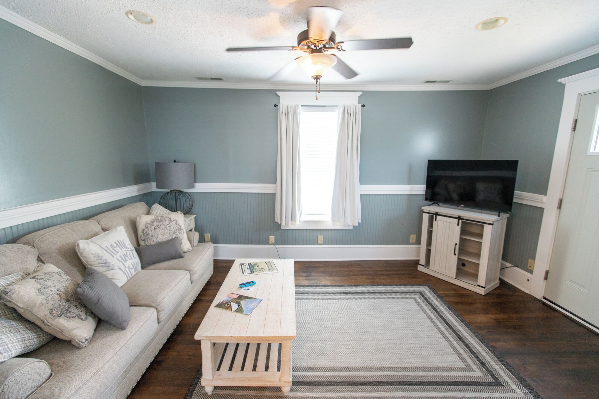 A living room with a sofa, coffee table, TV stand, and ceiling fan.