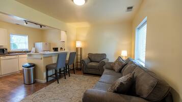 A compact living space with a kitchenette, a sofa, a chair, and a lamp.