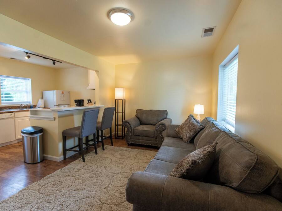 A compact living space with a kitchenette, a sofa, a chair, and a lamp.