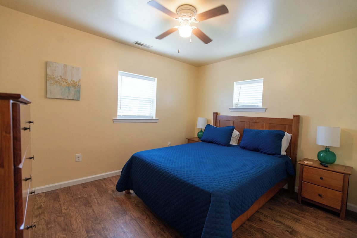 A bedroom with a bed, two nightstands, a ceiling fan, and two windows.