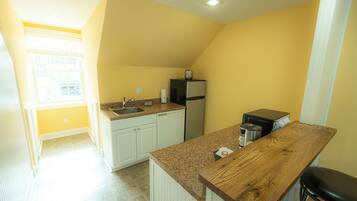 A compact kitchen with white cabinets, a granite countertop, a refrigerator, and a coffee maker.