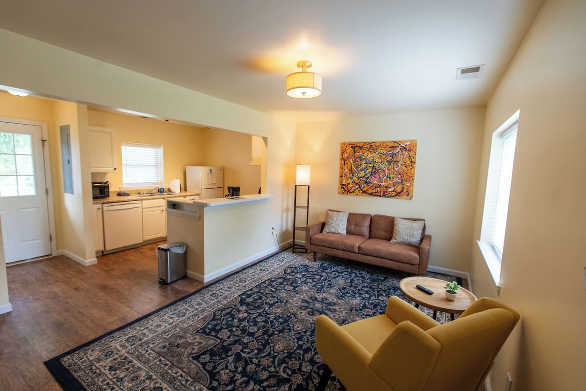 A modern kitchen with white cabinets, a central island, and a dining area with a yellow chair and a small table.