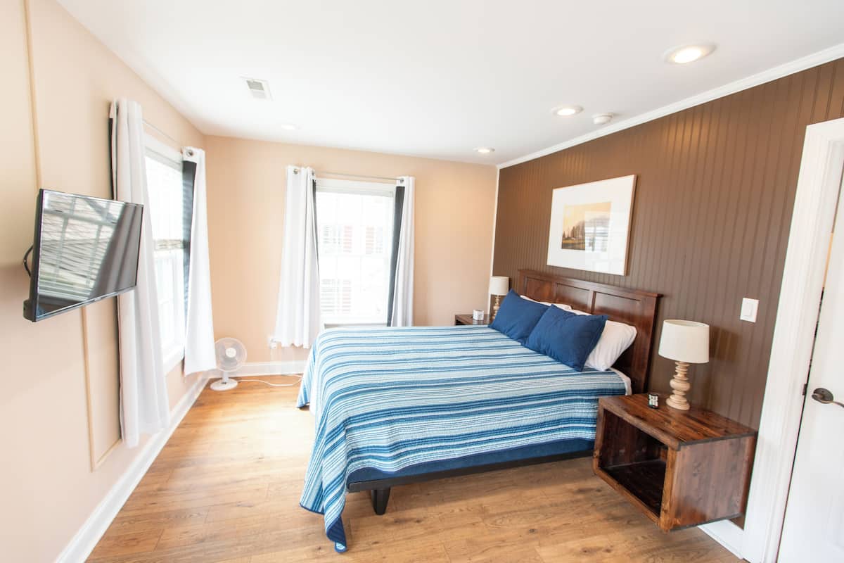 A bedroom with a bed, bedside tables, a TV, and a window with curtains.
