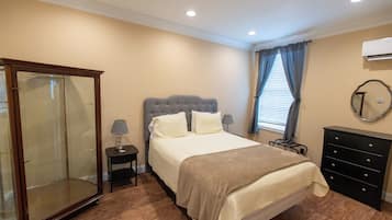 Un dormitorio con cama, armario, cómoda, mesita de noche con lámparas y ventana con cortinas.