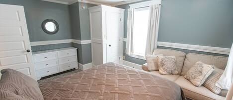 A bedroom with a large bed, a dresser, a ceiling fan, and a window with curtains.