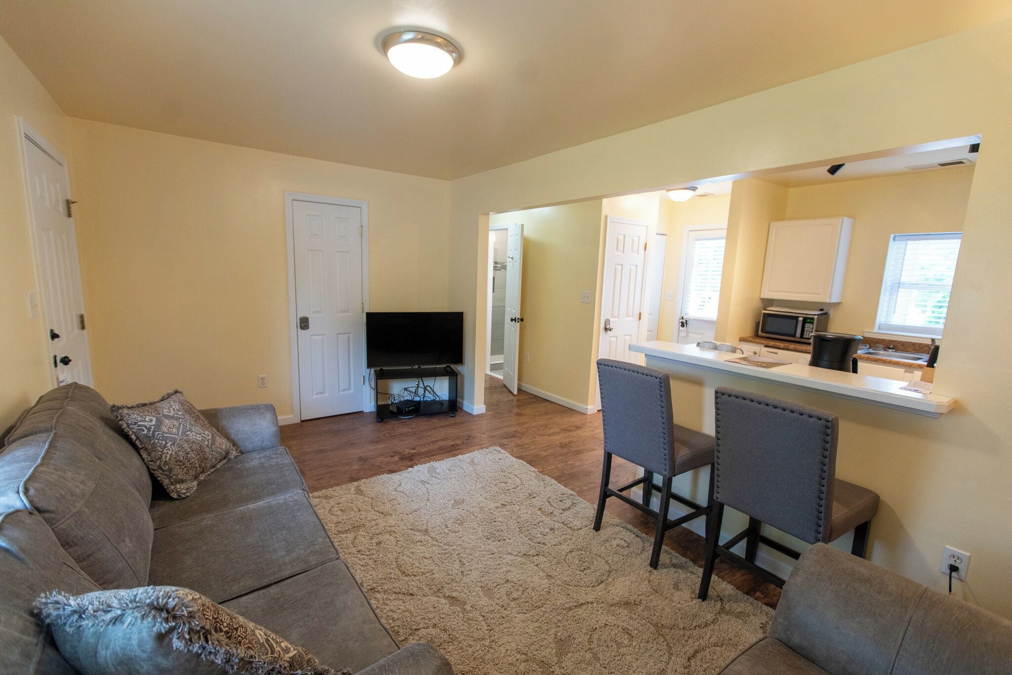 A living room with a sofa, two chairs, a flat-screen TV, and a kitchen area with a microwave.