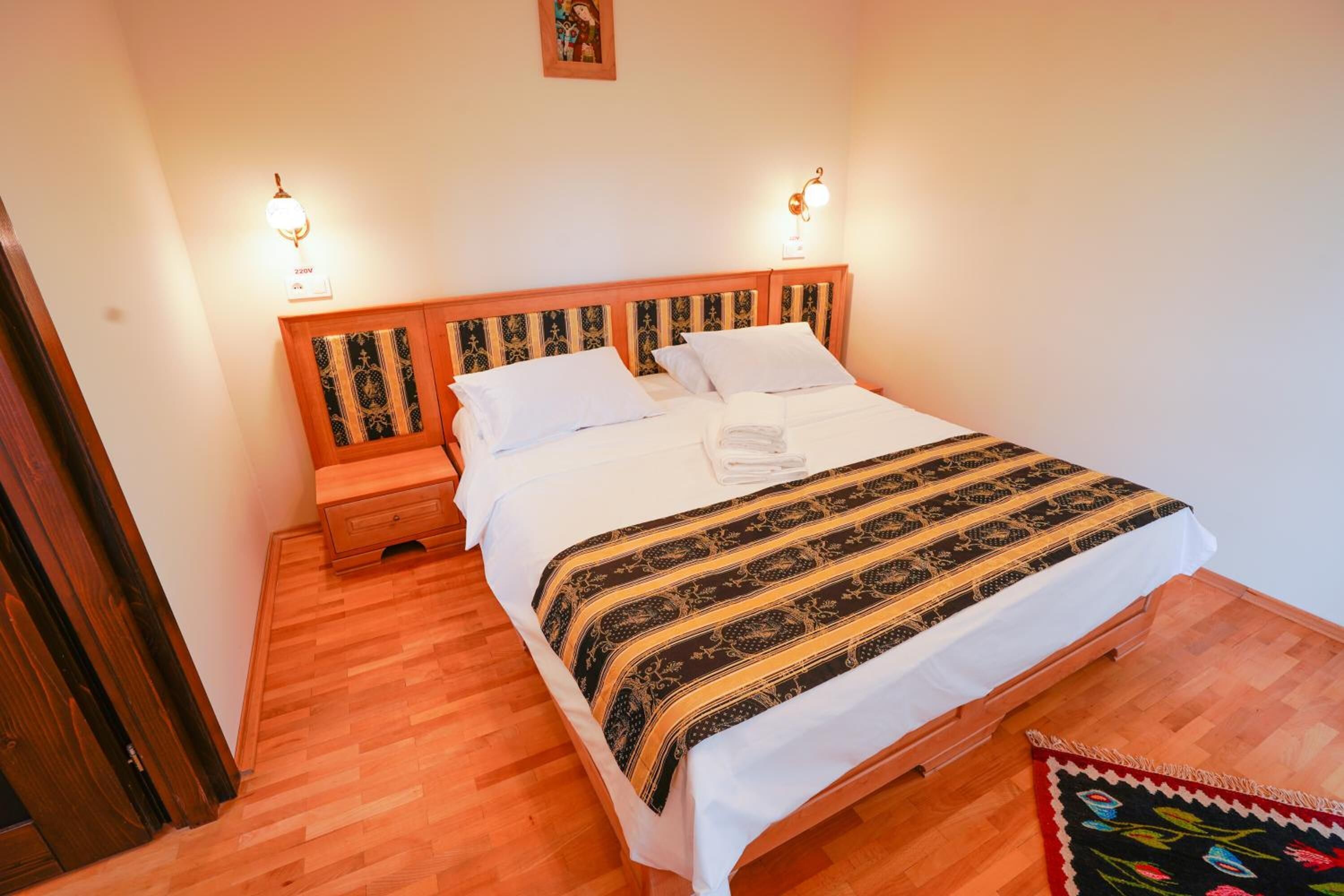 A double bed with a patterned bedspread, two bedside tables with lamps, and a wooden floor.