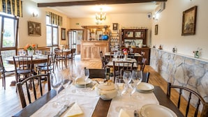 A dining area with multiple tables set for a meal, a bar area with bottles, and a stone wall. - Felix Pension (Prajila)