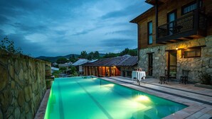 Una piscina con un muro de piedra en un lado y un edificio de madera con un balcón en el otro.