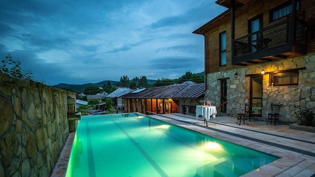 A swimming pool with a stone wall on one side and a wooden building with a balcony on the other. - Felix Pension (Prajila)