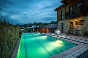 A swimming pool with a stone wall on one side and a wooden building with a balcony on the other. - Felix Pension (Prajila)