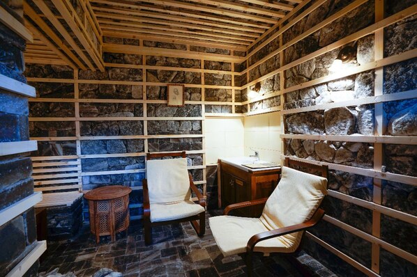 A stone-walled room with wooden beams, two chairs, a small round table, and a sink. - Felix Pension (Prajila)