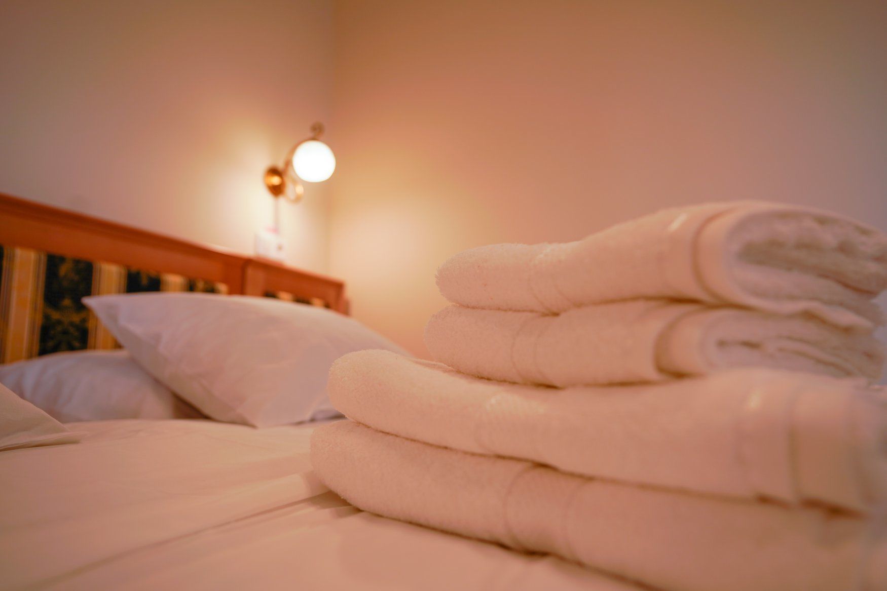 Una cama bien hecha con toallas dobladas y una lámpara de pared.