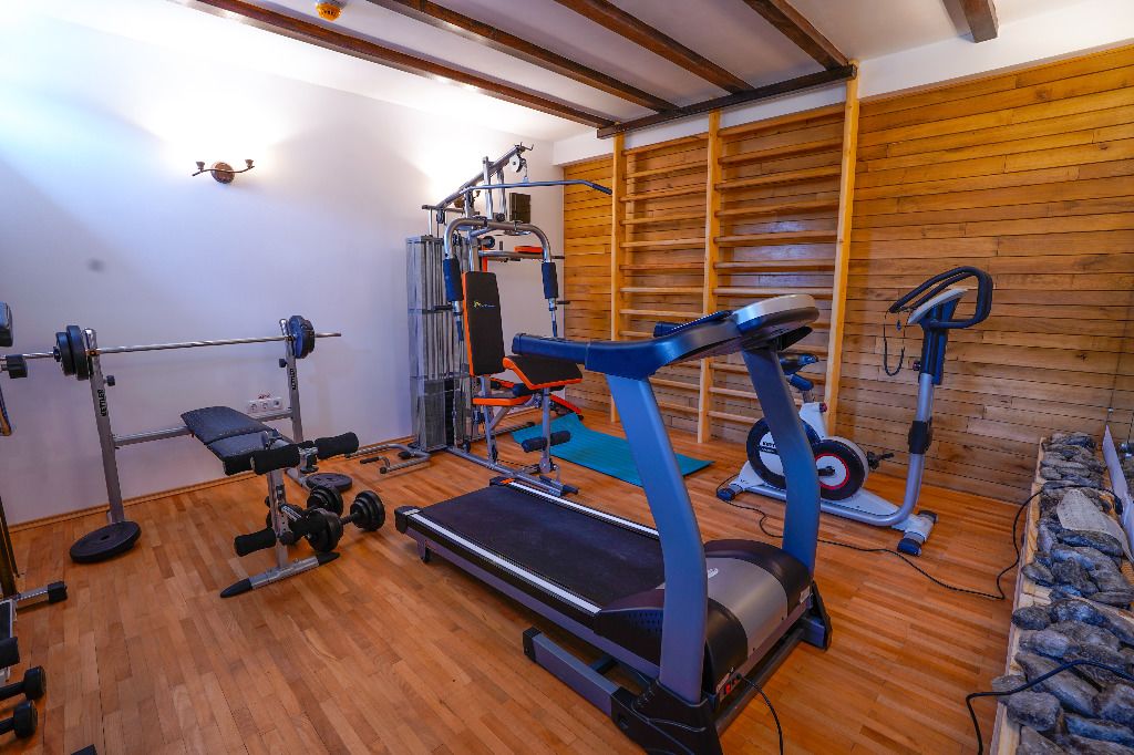 Uma academia com esteira, banco de musculação e diversos equipamentos de exercícios.