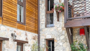 A stone building with wooden paneling, multiple windows, and a small garden area with flowers and plants. - Felix Pension (Prajila)