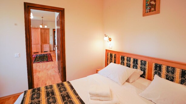 Una habitación de hotel con una cama, una mesita de noche, una lámpara de pared, una puerta con letrero de salida y un pasillo que lleva a un baño.