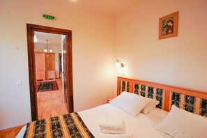 A hotel room with a bed, a nightstand, a wall-mounted light, a door with an exit sign, and a hallway leading to a bathroom.