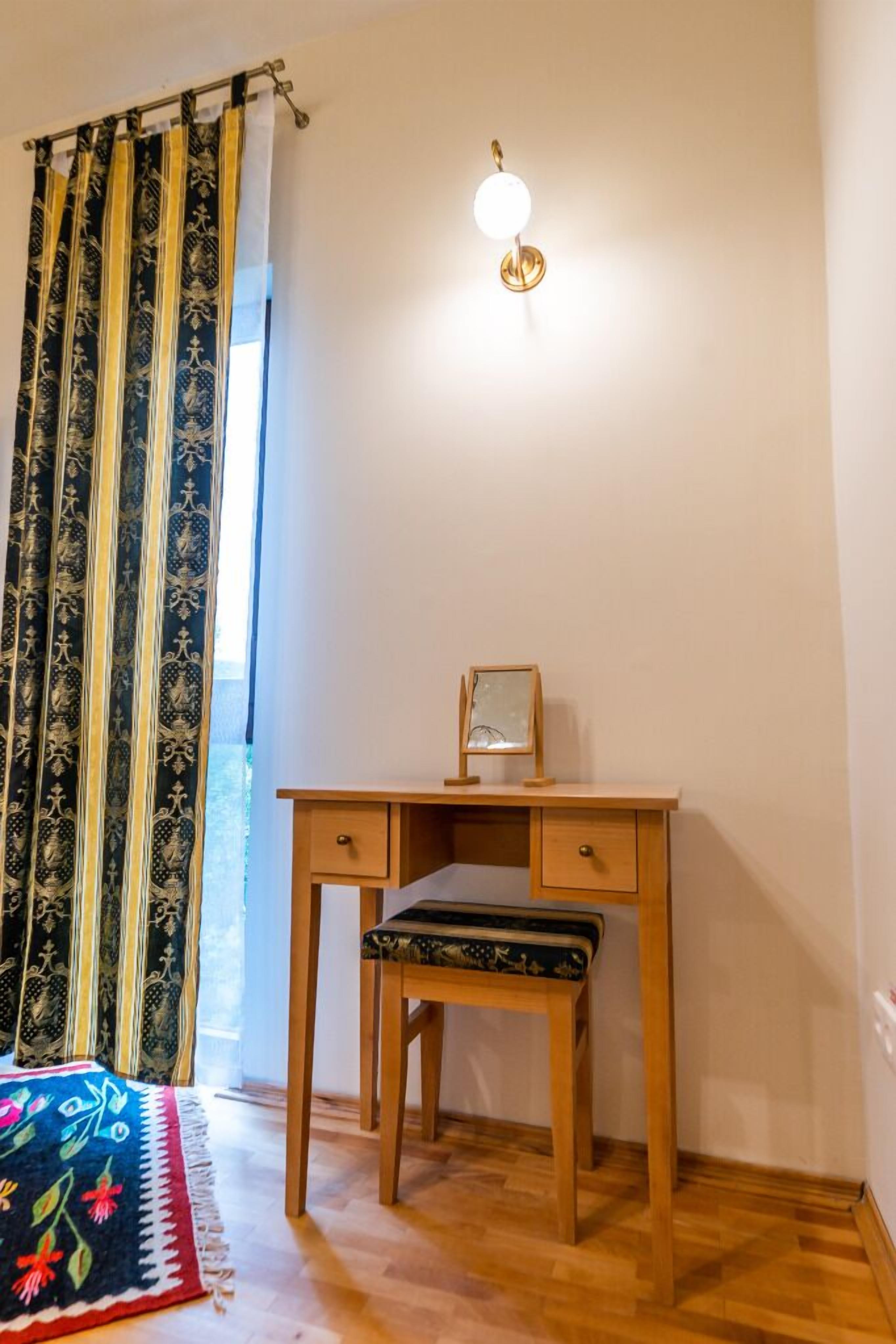 A room with a wooden desk, a chair, a small table with a framed picture, and a patterned rug on the floor.