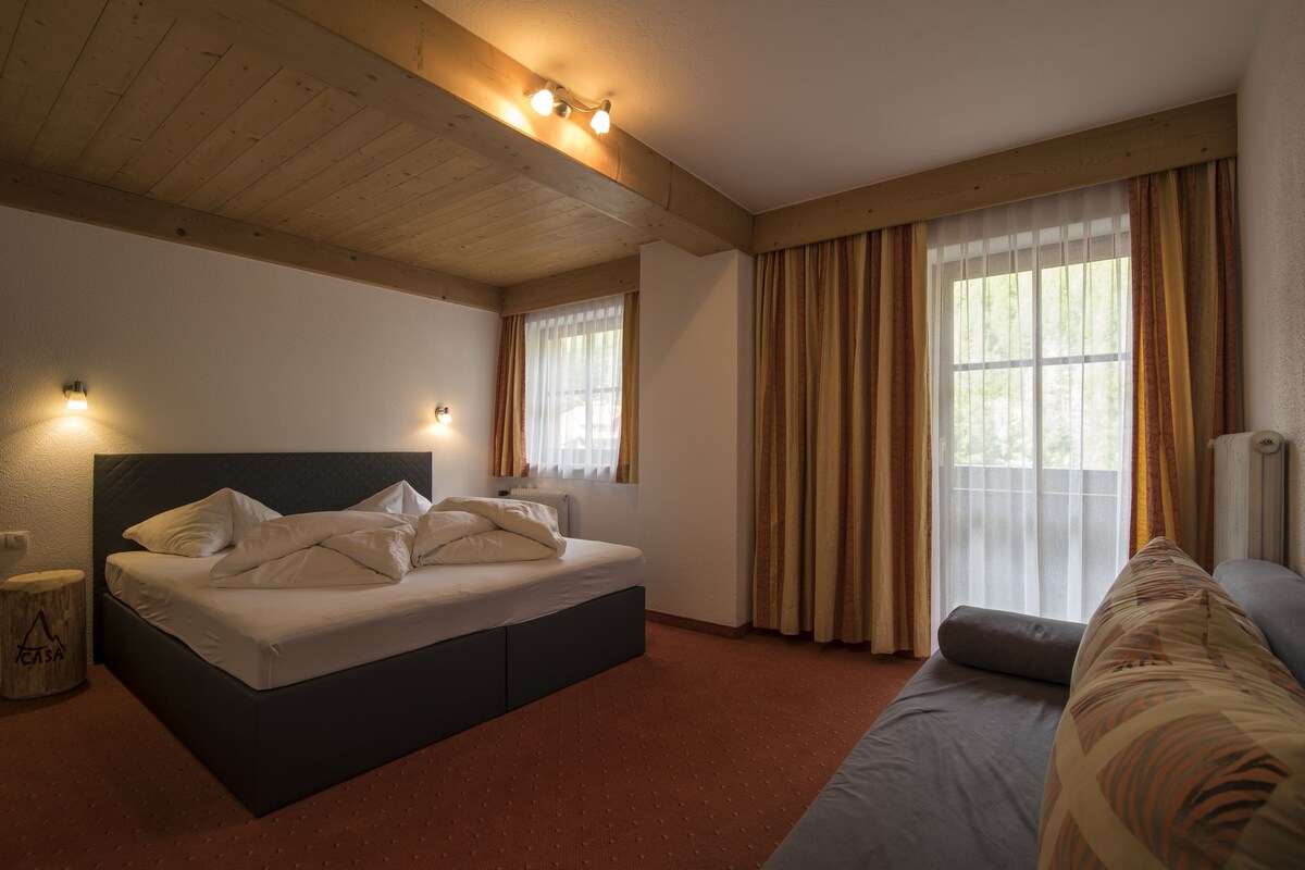 A bedroom with a bed, a sofa, and a window with curtains.